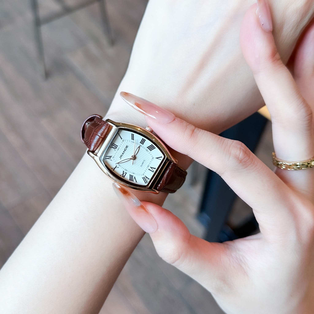 Women's bronze-tone quartz watch with white dial and brown leather strap on wrist.